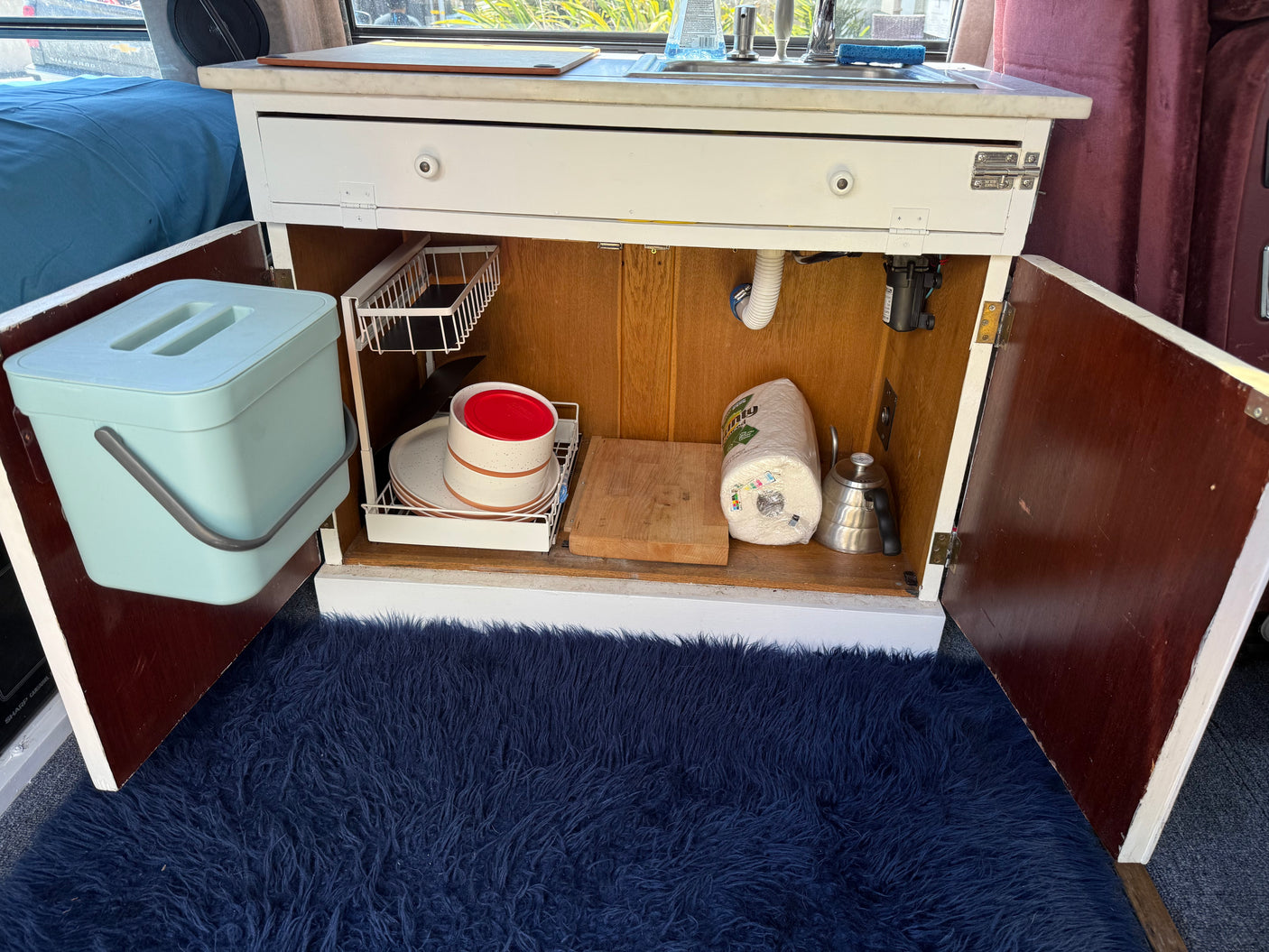 Organized rv rental kitchenette cabinets. Features include a compost bin, dish rack, cutting board, kettle, and sink area.