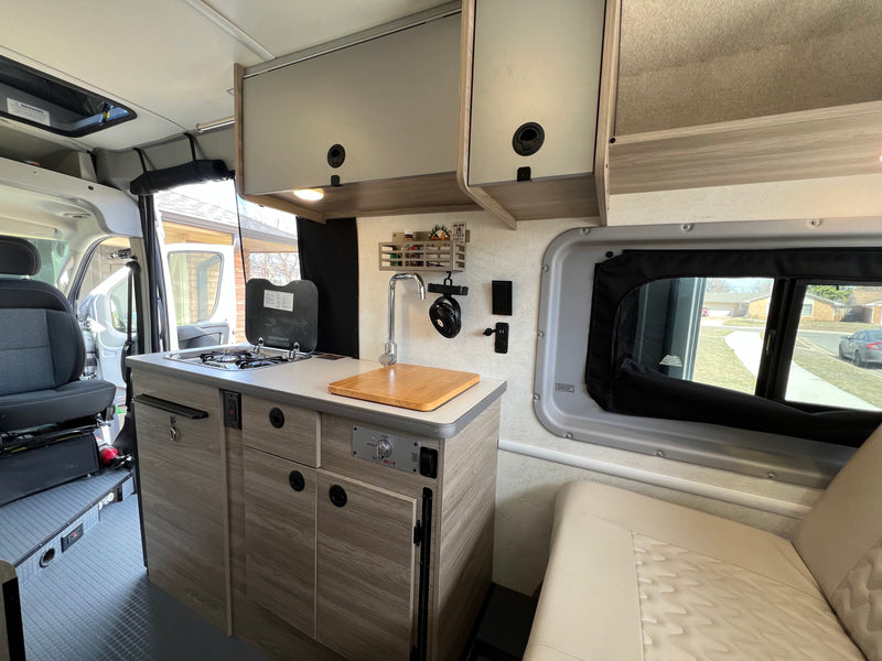 A bright, compact RV rental interior featuring a modern kitchenette with stove and sink, plus a cozy seating area. — photo 4