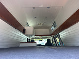 RV rental interior shows a converted campervan with white paneling, wood trim, bed, and ceiling fan, looking forward.