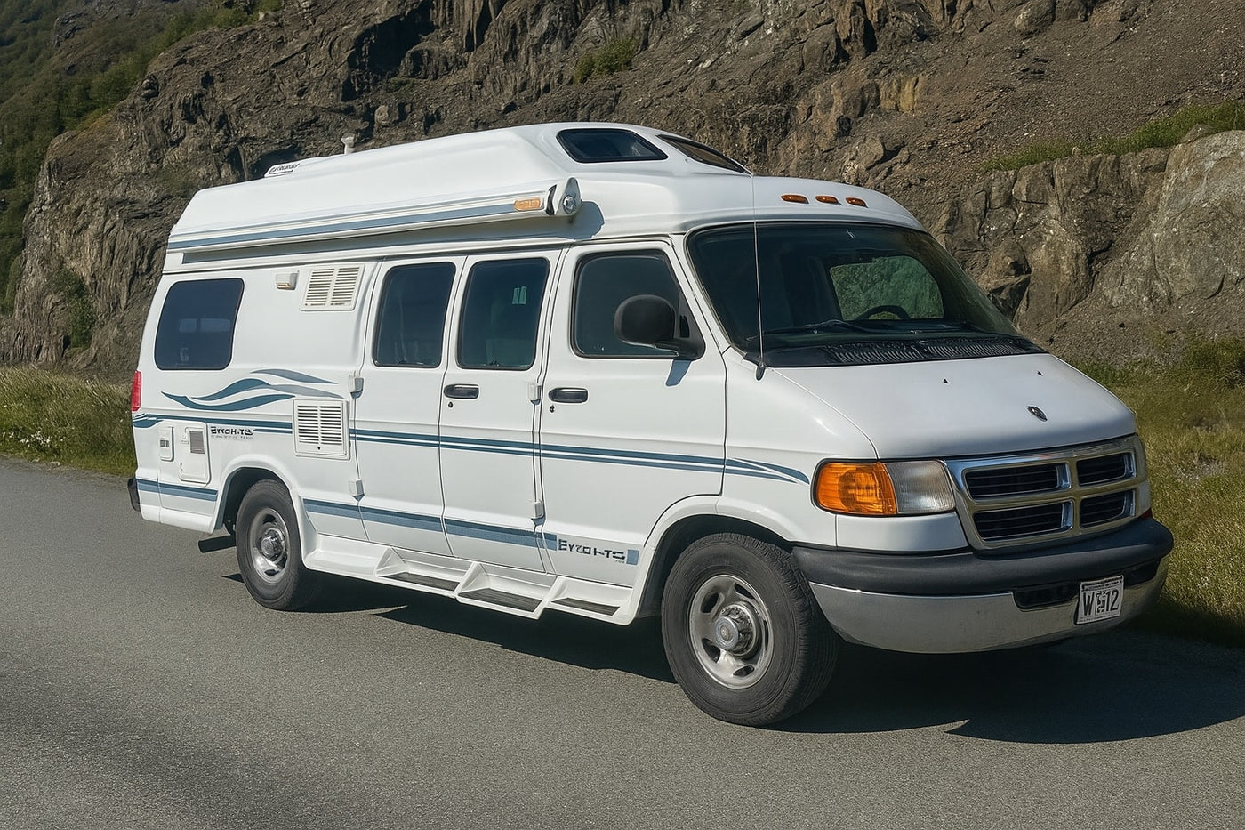 A white camper van, an ideal RV rental, is parked on a paved road with rocky cliffs and green vegetation in the background. — photo 8