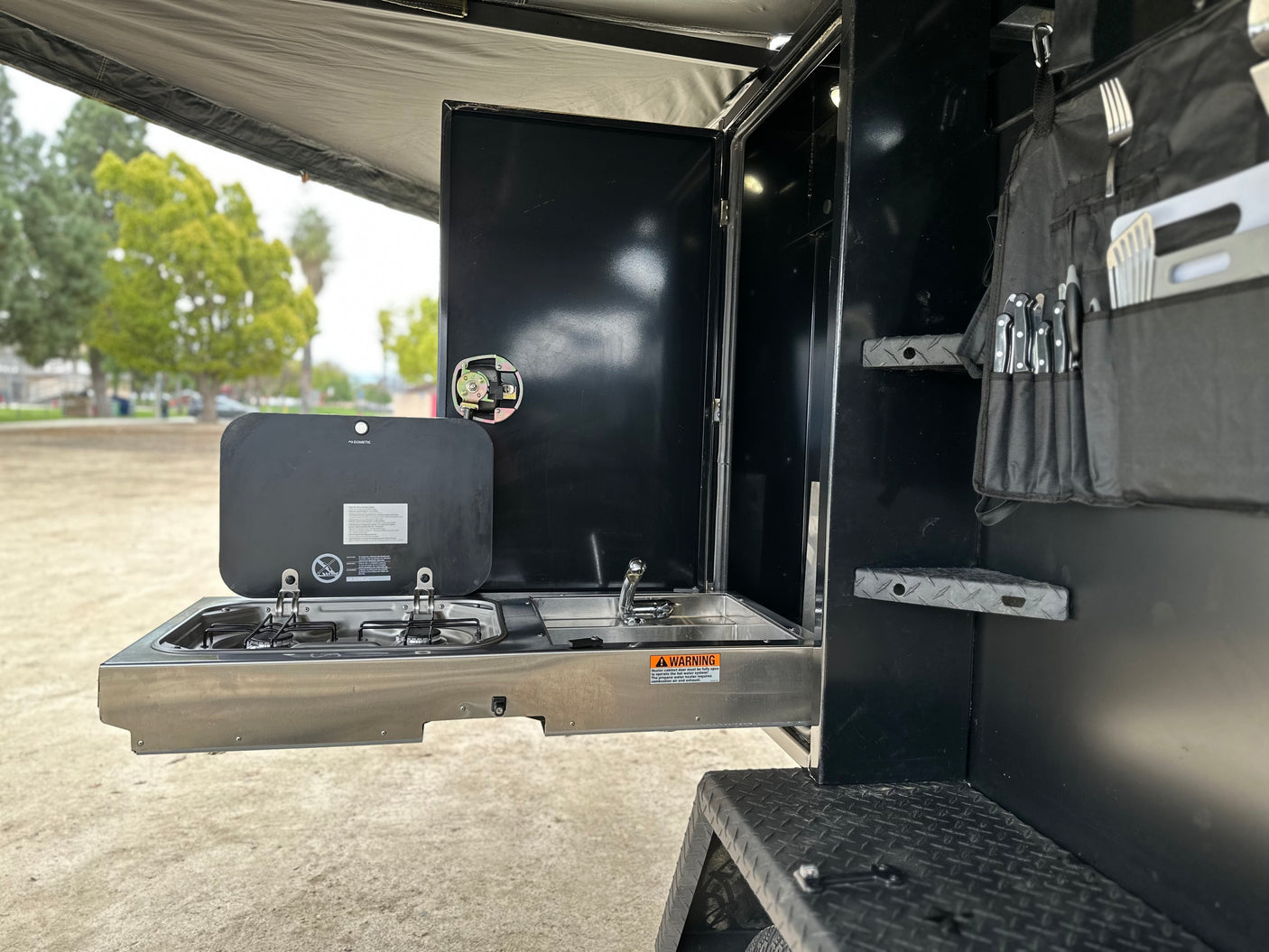 This RV rental features a pull-out Dometic outdoor kitchen with stove, sink, and utensil storage, ideal for camping.