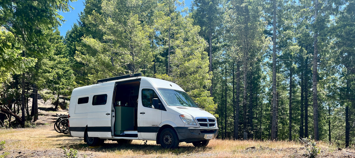 White RV rental camper van in a sunny forest. Bicycles mounted on back for outdoor adventures.
