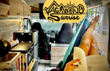 Cozy RV rental: person reading in a hammock inside a camper van, kitchen and nature views visible.