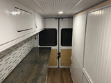 Bright RV rental conversion van interior with white ceiling, custom cabinets, patterned walls, and wood flooring.