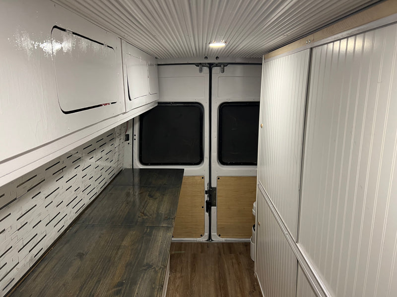 Bright RV rental conversion van interior with white ceiling, custom cabinets, patterned walls, and wood flooring. — photo 5
