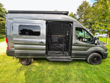 A sleek grey conversion van, set up as an RV rental, parked on grass with its side screen door open for fresh air.
