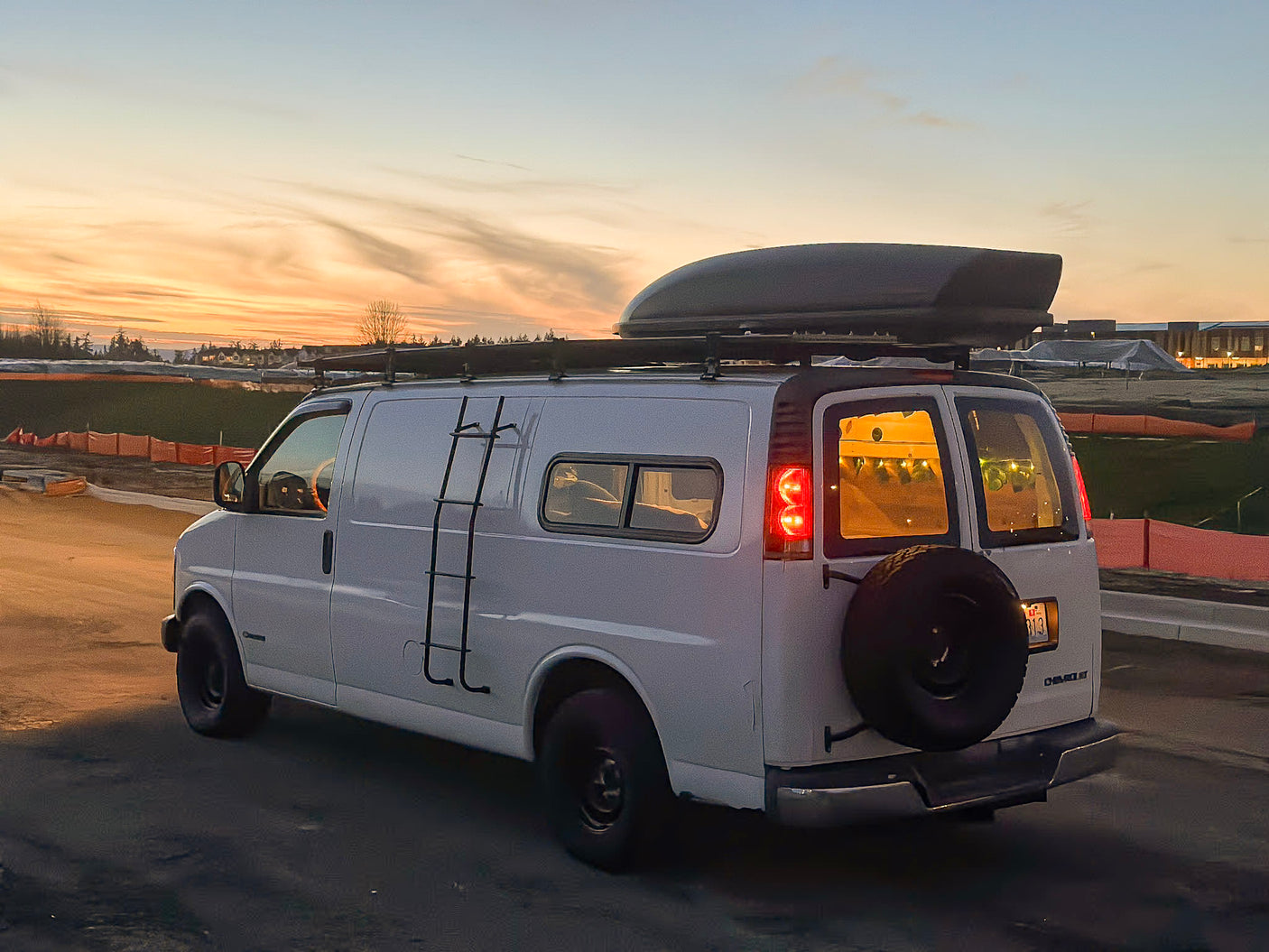 White modified Chevy van with roof box & rear tire mount, perfect for rv rental adventures at sunset.