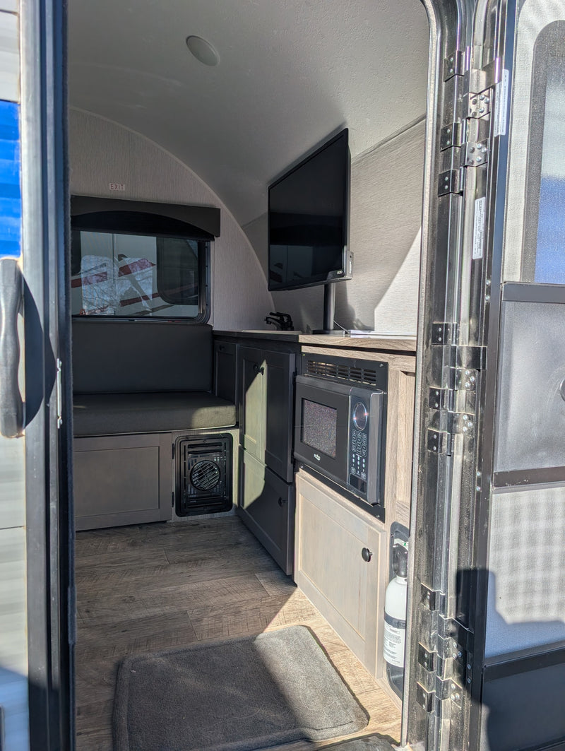 Inside an RV rental, showing the kitchenette with microwave, TV, dinette, and a fire extinguisher by the open door. — photo 8
