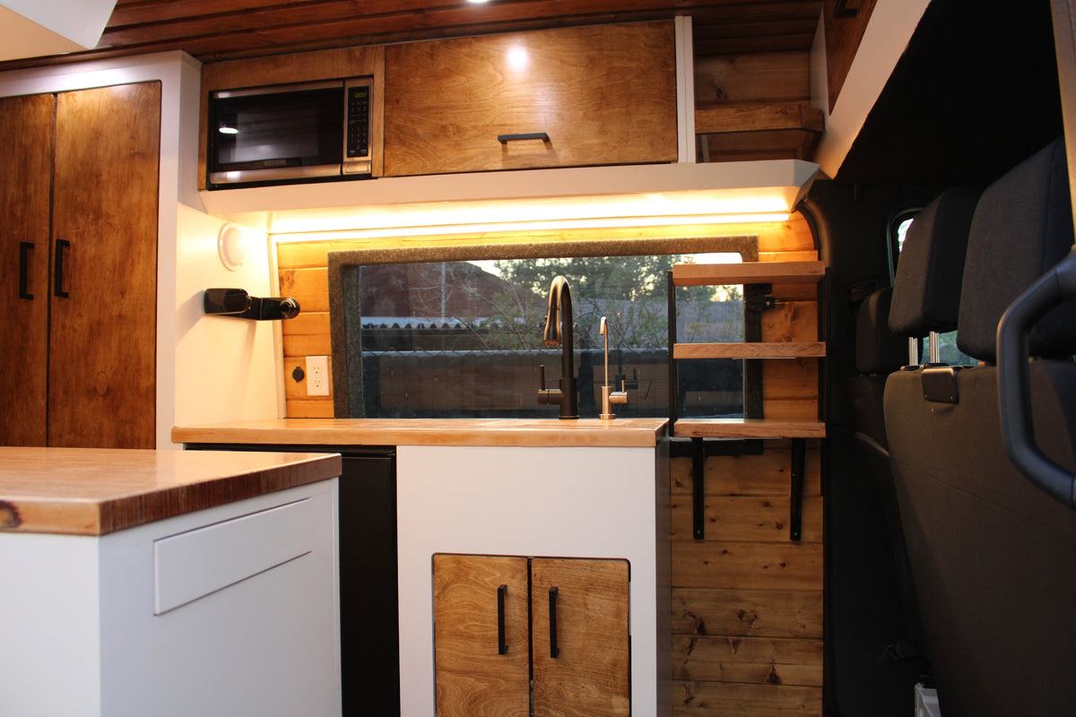 Cozy RV rental kitchen: wood cabinets, light counters, sink, microwave, and ambient lighting in a sleek van conversion. — photo 3