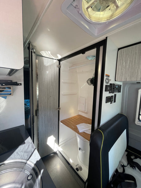 RV rental interior featuring a compact bathroom with shower/toilet, small kitchenette, and wall-mounted control panel.