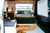 A woman relaxes in a comfortable RV rental, enjoying a game projected on a screen in her custom mobile living space.