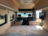 RV rental's interior features a comfy bed, kitchen, and TV. Enjoy the ocean view from this mobile adventure van.