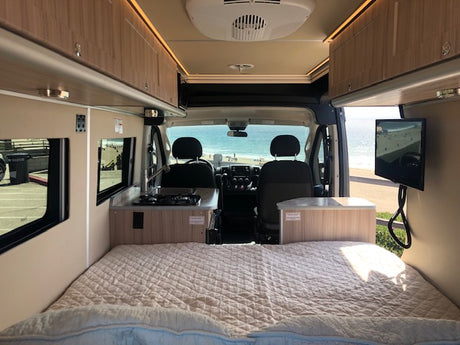 RV rental's interior features a comfy bed, kitchen, and TV. Enjoy the ocean view from this mobile adventure van.