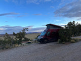 Adventure awaits! This red RV rental is parked in a scenic desert landscape with mesas and a blue sky, perfect for camping.