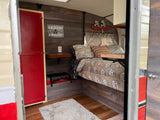 Experience a unique RV rental: wood-paneled interior, "Happy Camper" bed, and playful decor for comfortable glamping.