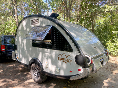 Shaded Boondock Lite teardrop RV rental next to an SUV, ready for adventure. Ideal for camping.