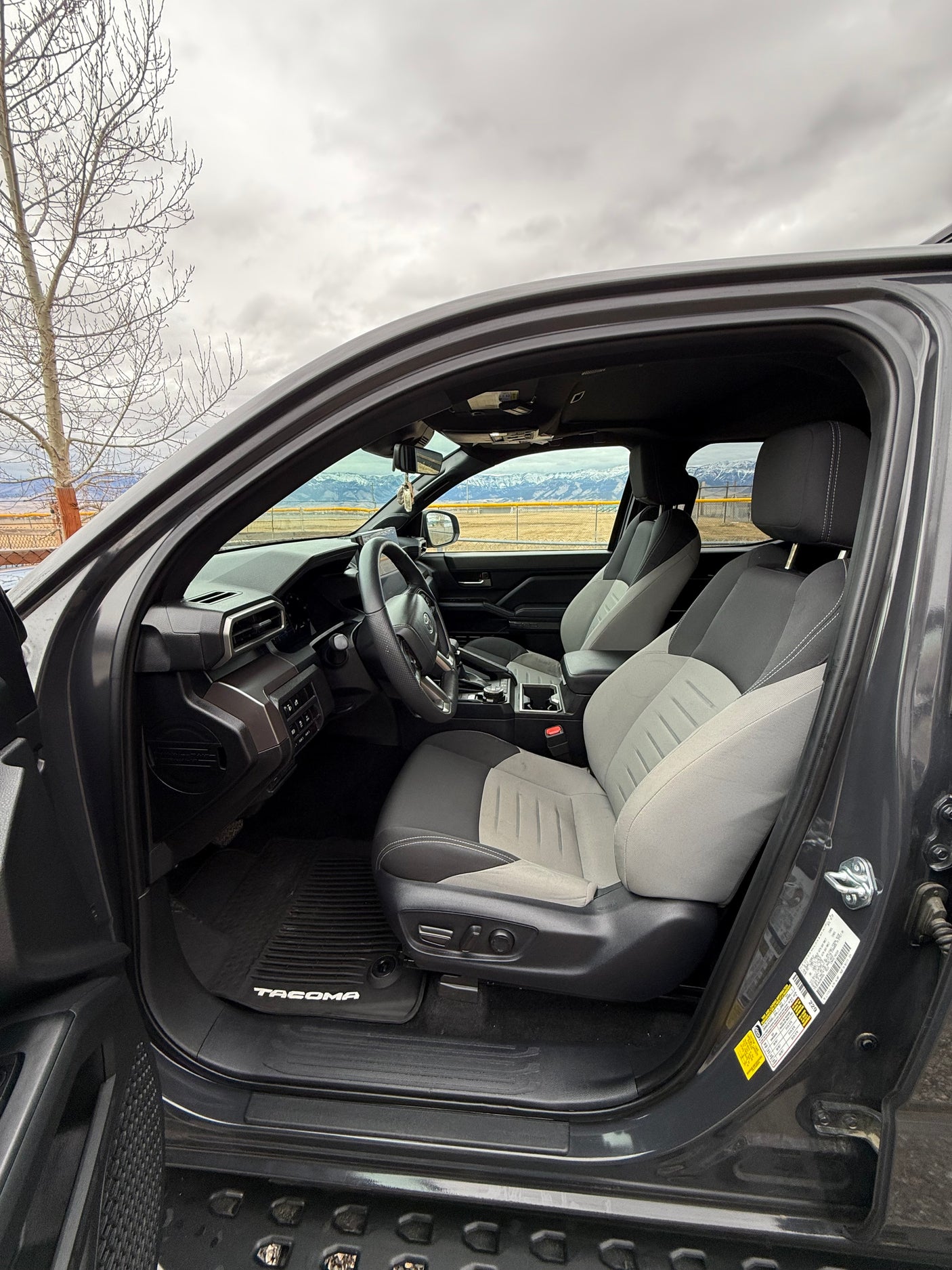 Driver's seat view of a Toyota Tacoma truck's gray/black interior, showing dashboard & steering wheel. Mountains beyond. Perfect for an rv rental trip.