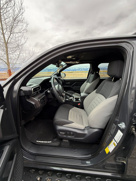 Driver's seat view of a Toyota Tacoma truck's gray/black interior, showing dashboard & steering wheel. Mountains beyond. Perfect for an rv rental trip.