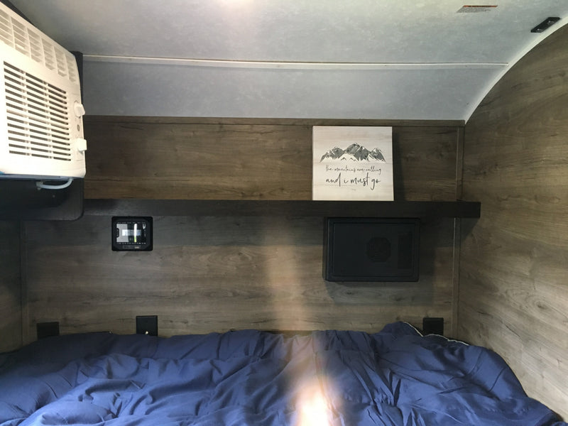 Cozy RV rental bedroom featuring a bed with blue covers, wall-mounted AC, electronic controls, and a shelf with mountain decor. — photo 9