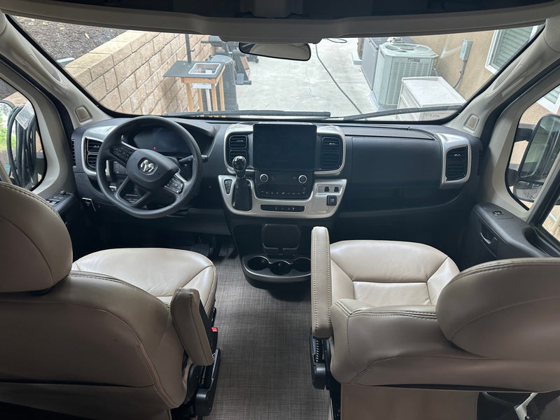 Inside this **rv rental**: beige leather driver and passenger seats, a sleek dashboard with screen, and wide front views. — photo 16