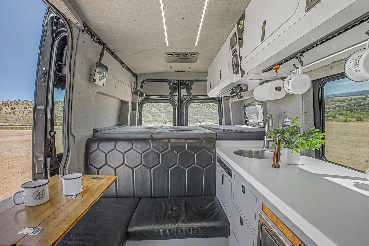 Interior of a luxurious camper van, showing a kitchen, dining bench, and bed setup. Ideal for an RV rental getaway.