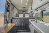 Interior of a luxurious camper van, showing a kitchen, dining bench, and bed setup. Ideal for an RV rental getaway.