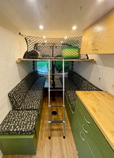 This rv rental's organized camper van interior features patterned seating, a ladder, overhead storage nets, and a compact kitchen.