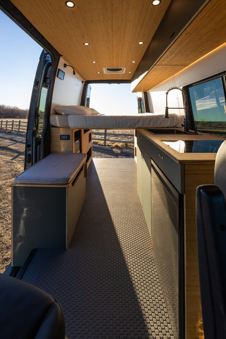 Explore this stylish RV rental! A spacious camper van interior featuring a comfortable bed, modern kitchen, and seating area.