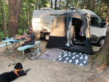 An RV rental campsite with a man preparing food, a screen tent setup, and two dogs relaxing nearby.