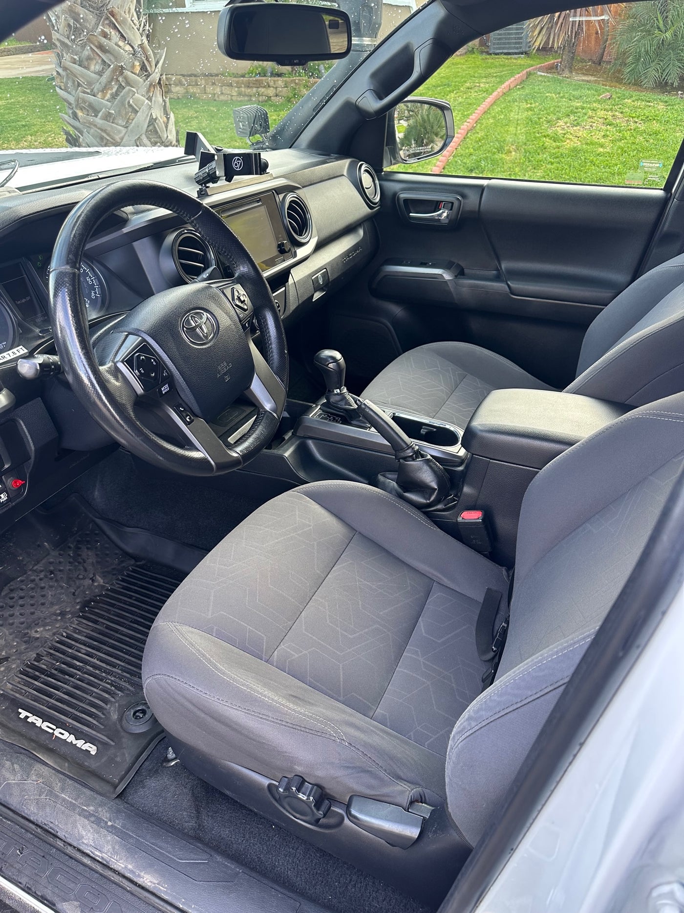 Spacious gray vehicle interior with steering wheel & dashboard. View of green yard outside. Perfect for trips, possibly with an rv rental. — photo 12