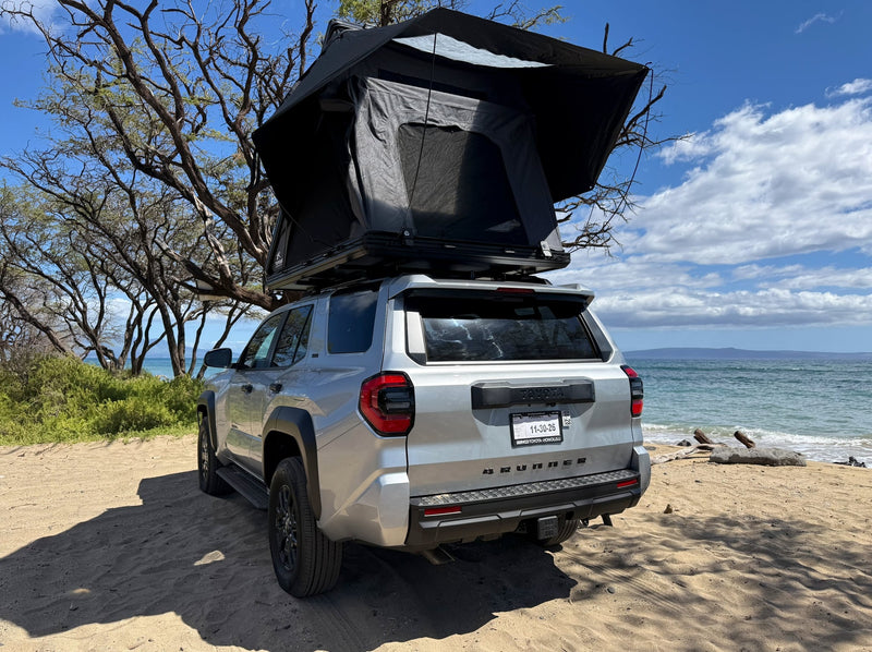  parked by the ocean on a sandy shore.|Experience beach camping with this RV rental: a silver Toyota 4Runner featuring a rooftop tent — photo 4