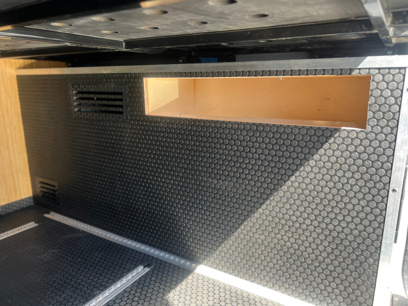 RV rental interior: black textured floor with cargo rails, a wooden storage cubby, and ventilation vents. — photo 20