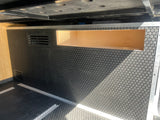 RV rental interior: black textured floor with cargo rails, a wooden storage cubby, and ventilation vents.