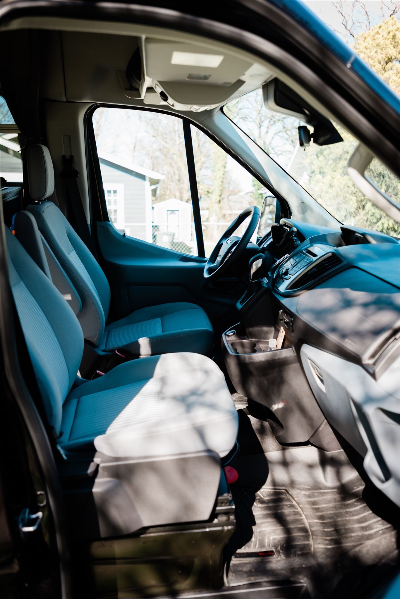 Inside an RV rental van: A spacious front cabin with light grey seats, dashboard, and a clear view out the windshield.