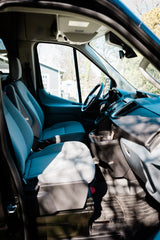 Inside an RV rental van: A spacious front cabin with light grey seats, dashboard, and a clear view out the windshield.
