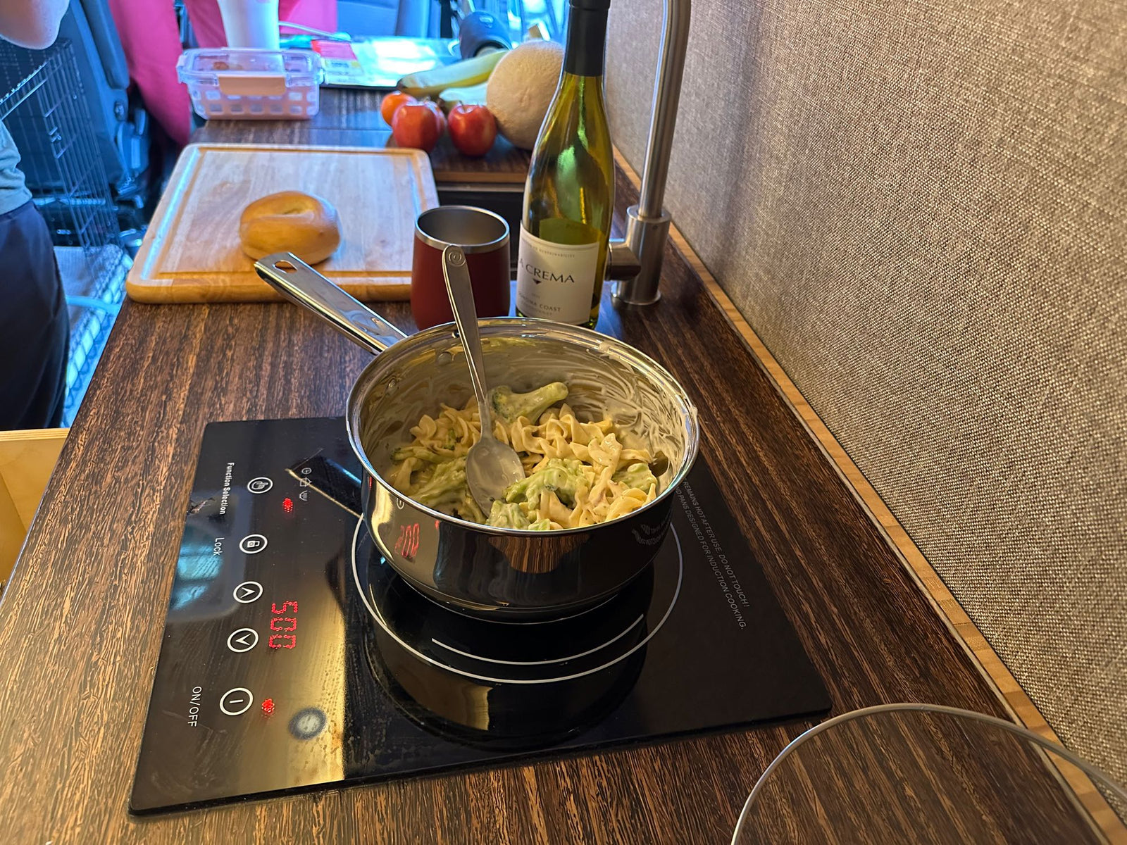 Enjoying a home-cooked meal in an RV rental, with pasta cooking on an induction cooktop, wine, and a bagel.