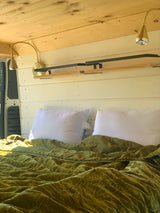 Inside an RV rental: a cozy bed with velvet green bedding, integrated lighting & wood features.
