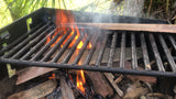 A black metal grill sits over a fiery campfire with smoke. Perfect for outdoor cooking on your RV rental adventure.