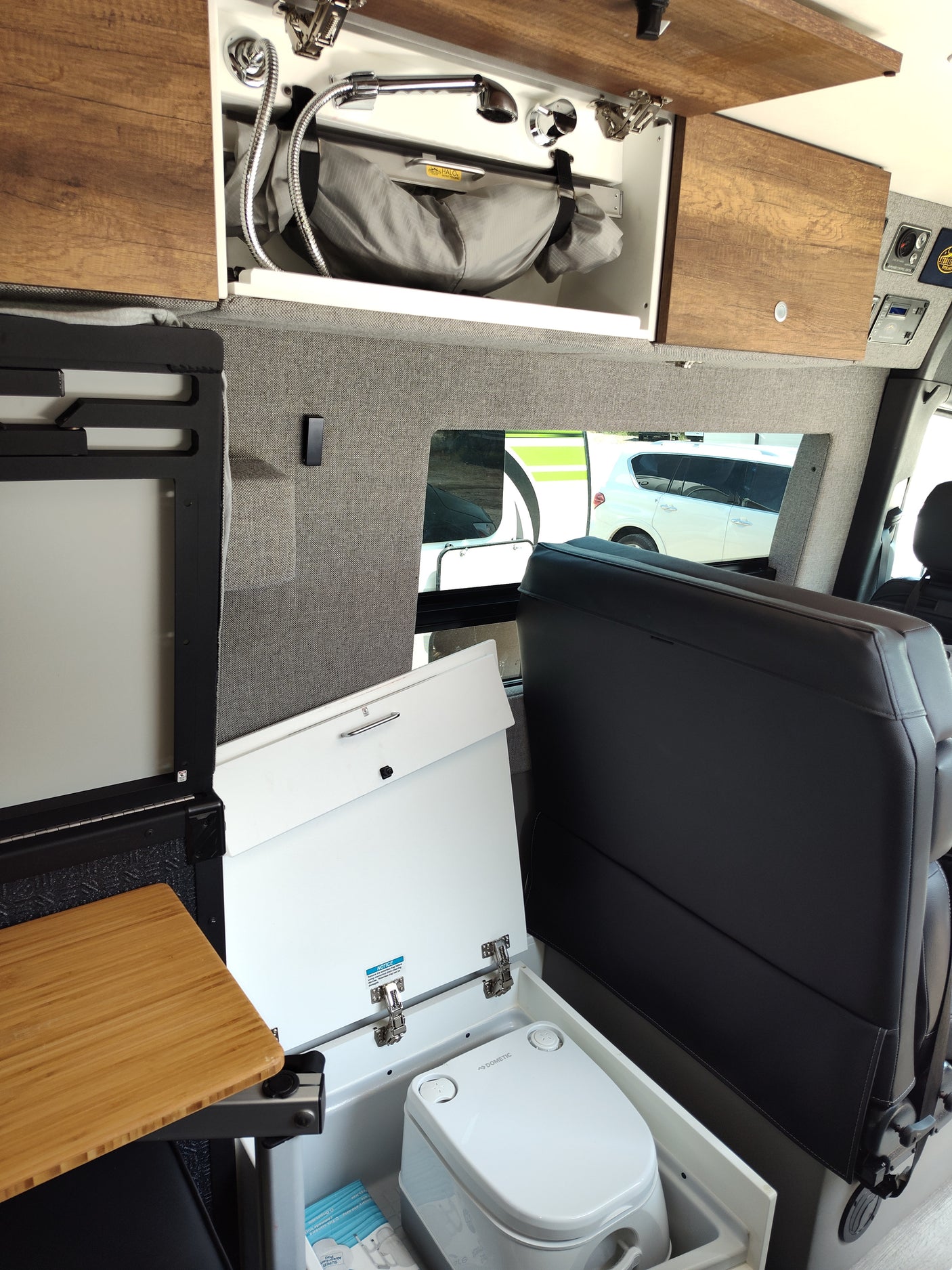 RV rental: Inside view of a camper van with overhead shower, Dometic portable toilet, and seating.
