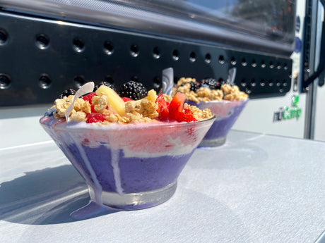 Layered smoothie bowls topped with fresh fruit and granola, enjoyed on an RV rental table outside.