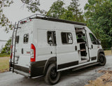 White camper van, perfect for RV rental, with open doors, ladder, and roof rack, parked by the lake.