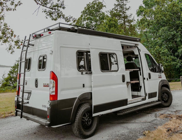 White camper van, perfect for RV rental, with open doors, ladder, and roof rack, parked by the lake.