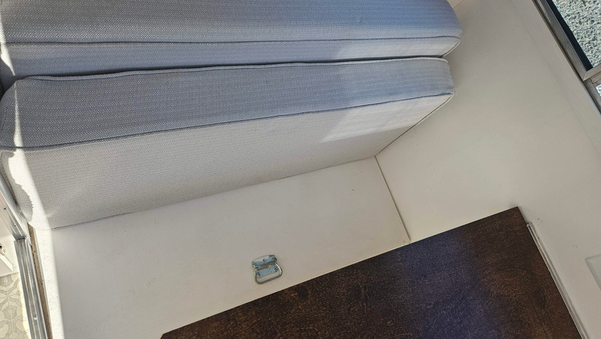 This RV rental interior features light gray cushions on white surfaces, with a dark brown table and a metal latch. — photo 12