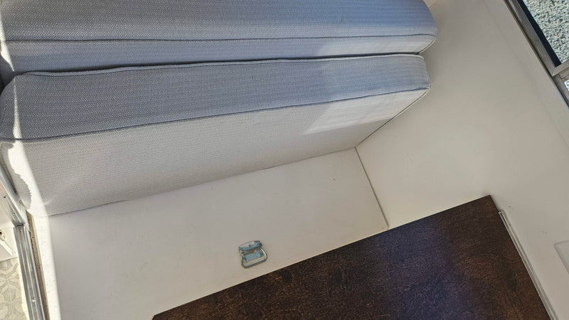 This RV rental interior features light gray cushions on white surfaces, with a dark brown table and a metal latch. — photo 12