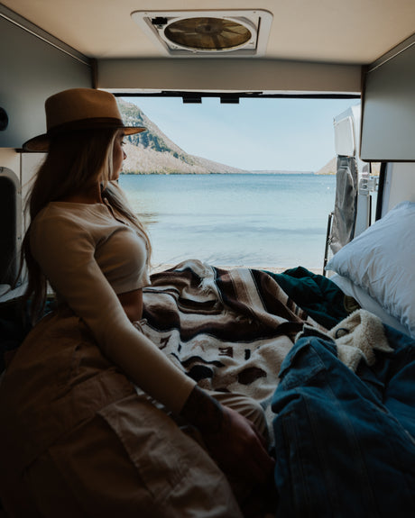 A woman in a hat gazes at a stunning lake view from inside her cozy RV rental, perfect for scenic adventures.