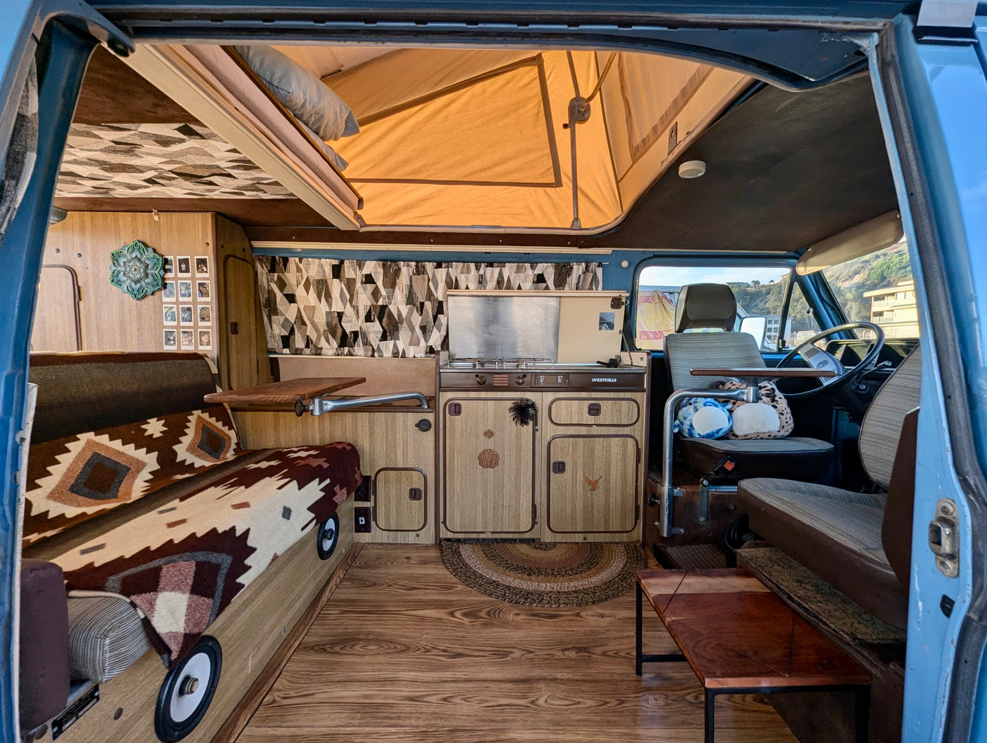 Interior view of a spacious RV rental camper van, featuring a pop-top, full kitchen, sleeping area, and wood flooring.