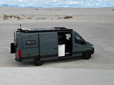 Adventure-ready grey camper van RV rental in the vast White Sands desert, ideal for off-grid trips.