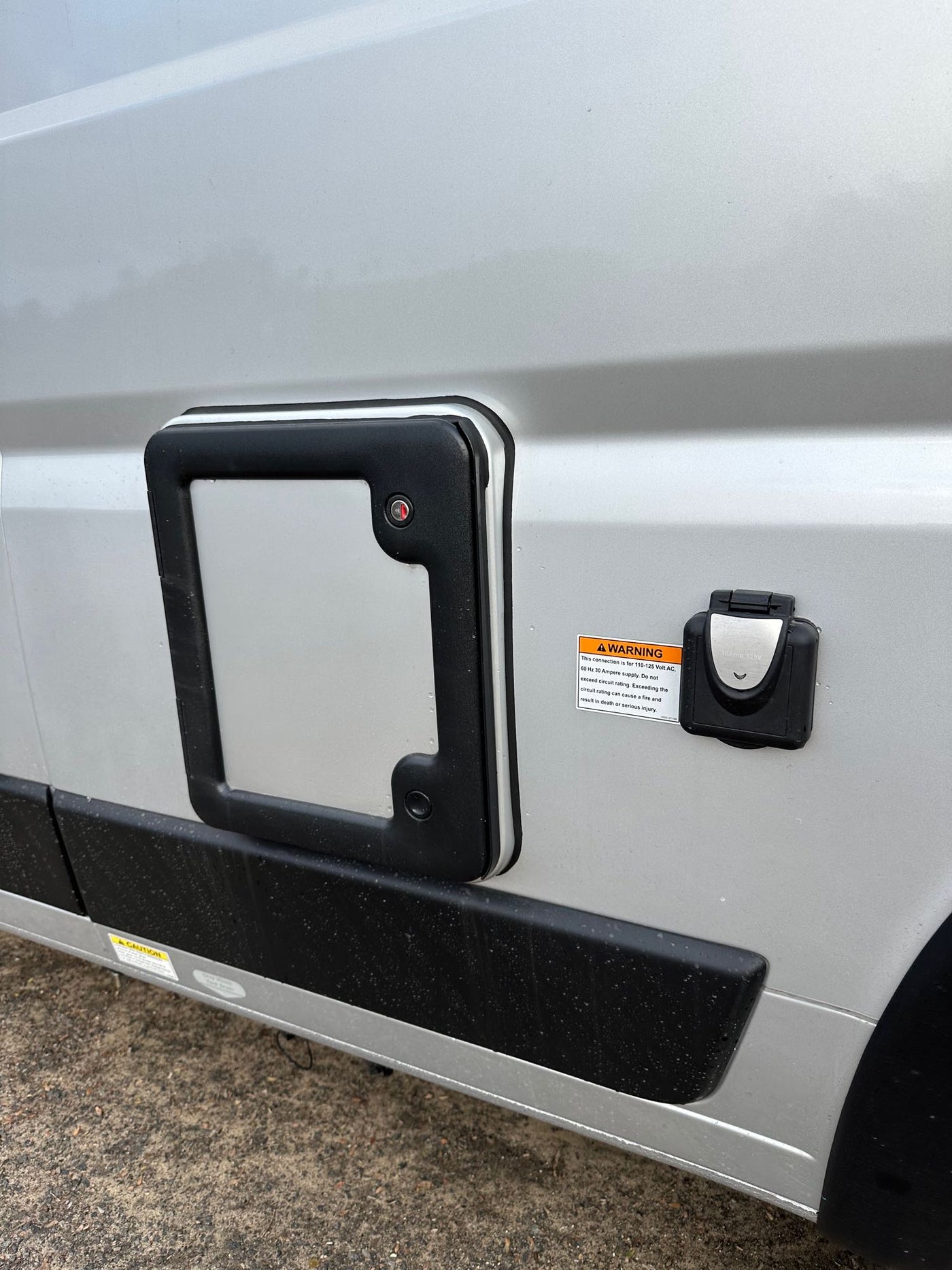  showing interior and sandals outside. Perfect for van life.|Side of an RV rental: external 30-amp electrical hookup with warning label and an access panel are visible on the silver exterior.|Inside an RV rental: rear view of a camper van with a bug screen — photo 4