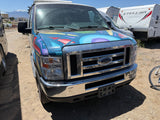 A custom-painted blue Ford van, possibly an RV rental, sits in a dusty lot with snowy mountains and other trailers.