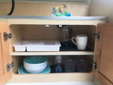 RV rental kitchen cabinet: Organized French press, mugs, bowls, plates, glasses, storage, and decorative birds in a boat.